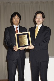 大鹿哲郎審査委員長(筑波大学人間総合科学研究科教授:左)から盾を受け取る加治准教授